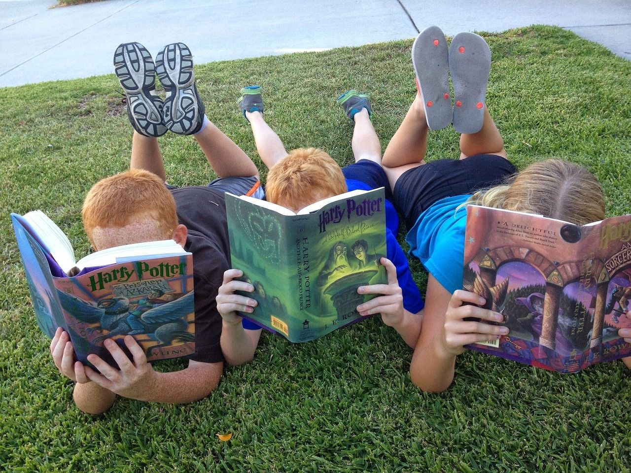 Kids lying on a lawn, reading Harry Potter books; boost reading skills concept