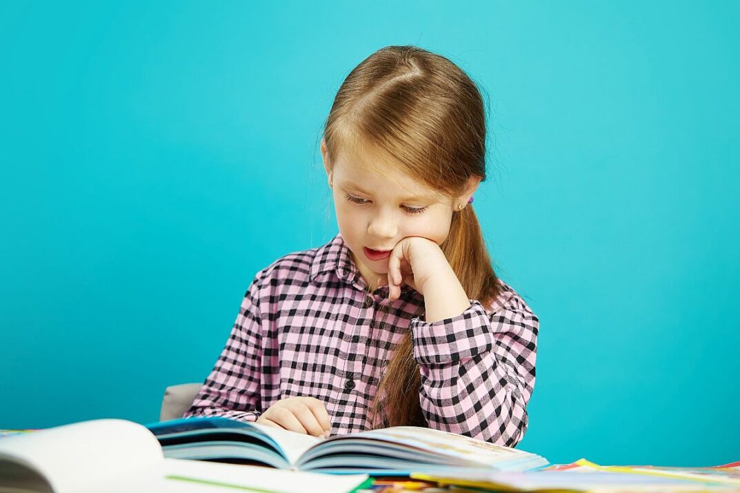 Child sitting at a table, reading a book; boost reading skills concept