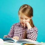 Child sitting at a table, reading a book; boost reading skills concept