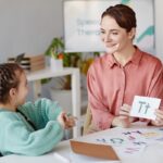 Woman showing alphabet card to young girl at table; reading specialists concept