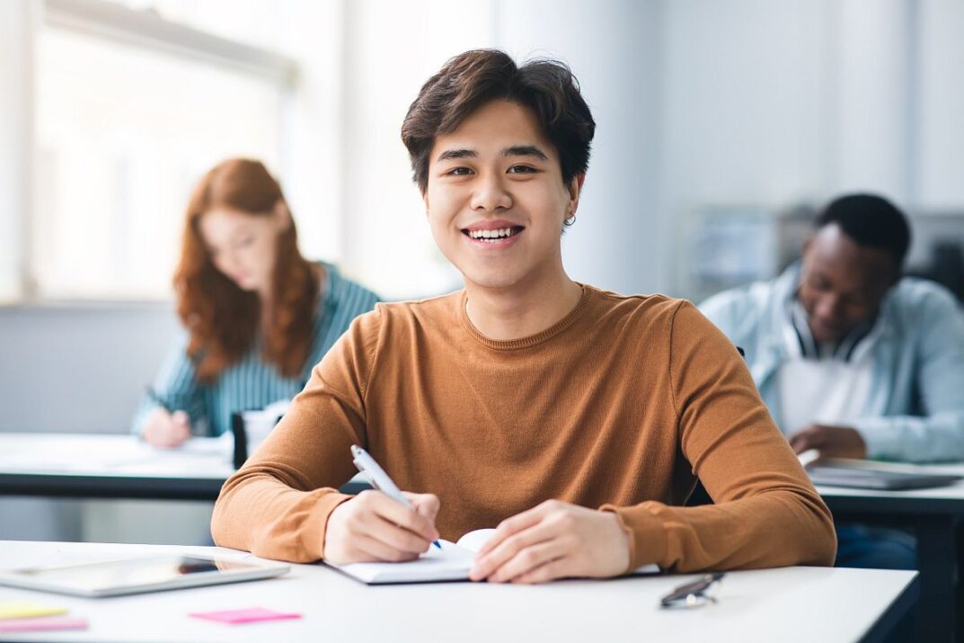 Smiling student looking up from writing; students writing skills concept