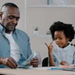 Man counting money with child; financial literacy concept