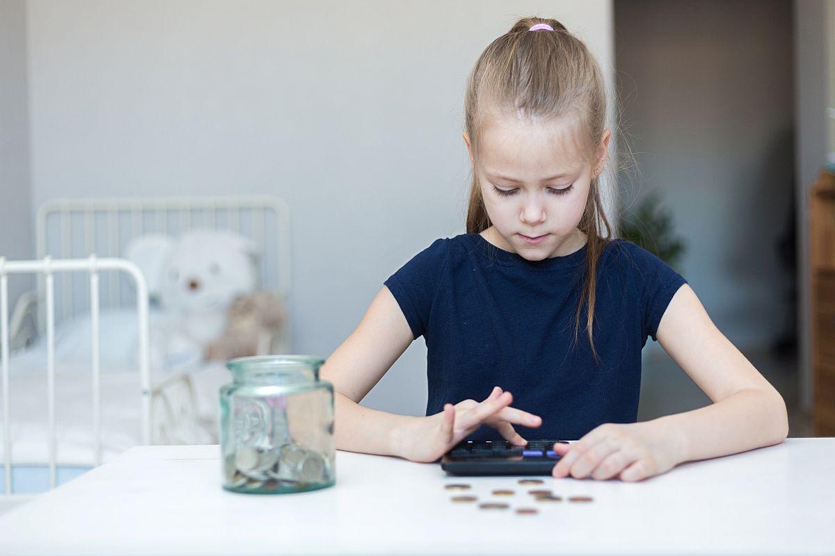 Girl using calculator to count coins; financial literacy concept