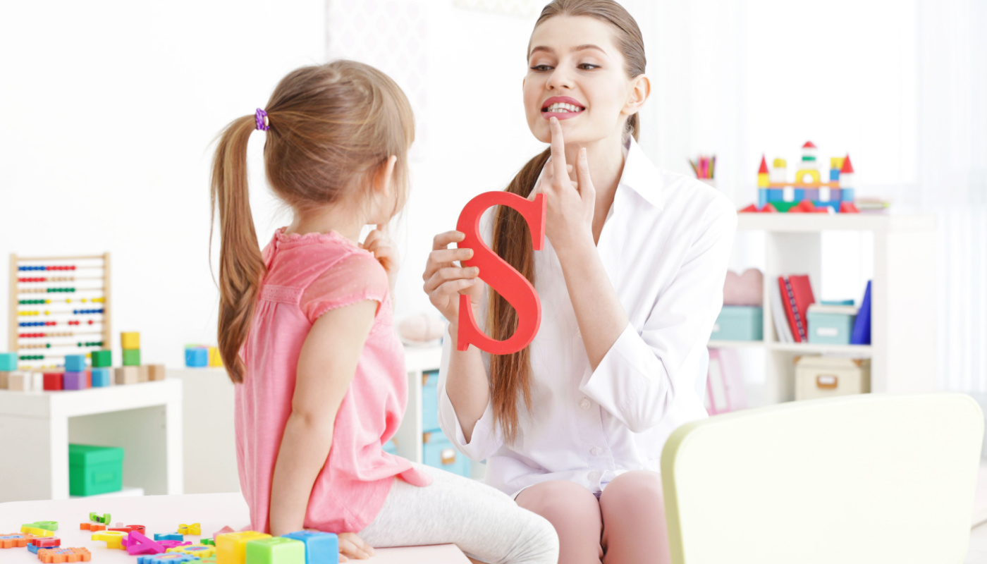 Speech therapist teaching little girl how to pronounce a sound; speech therapists concept