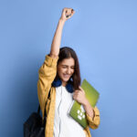 Young girl holding book, raising one hand in triumph; self-study concept