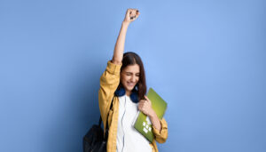 Young girl holding book, raising one hand in triumph; self-study concept