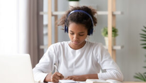 Girl with headphones and laptop writing in book; How Much Homework concept