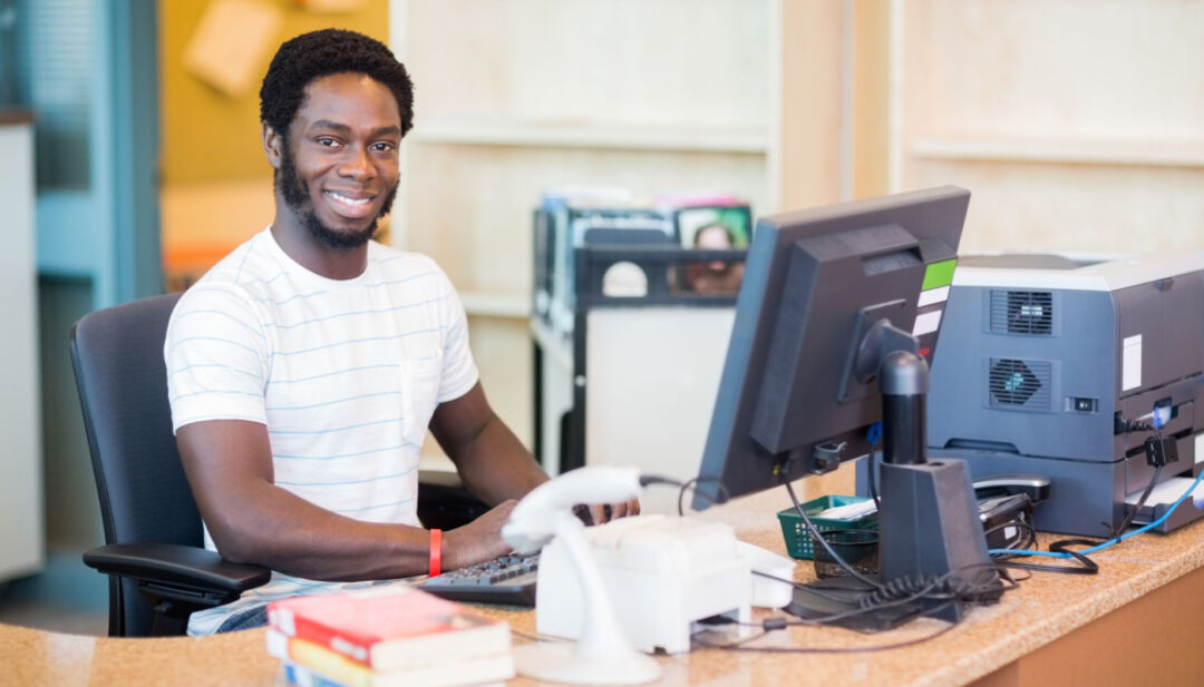 Smiling man sitting at desk in library; school librarians concept