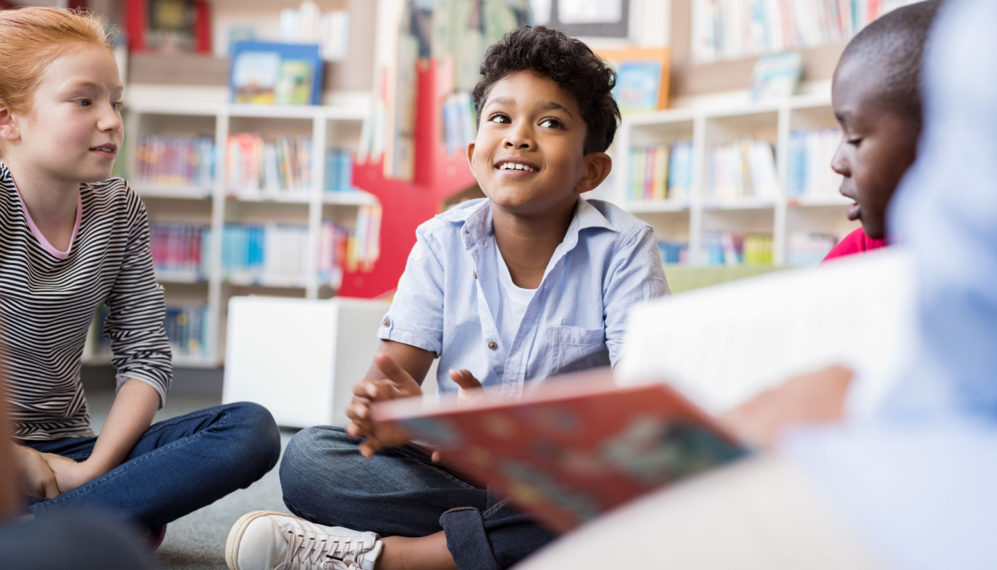 Children sitting on floor listening to adult read; school librarians concept