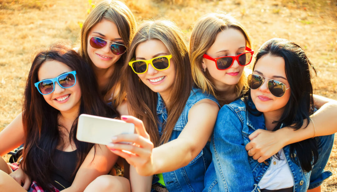 Group of girls in sunglasses taking a selfie; social media and body image concept