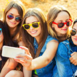 Group of girls in sunglasses taking a selfie; social media and body image concept
