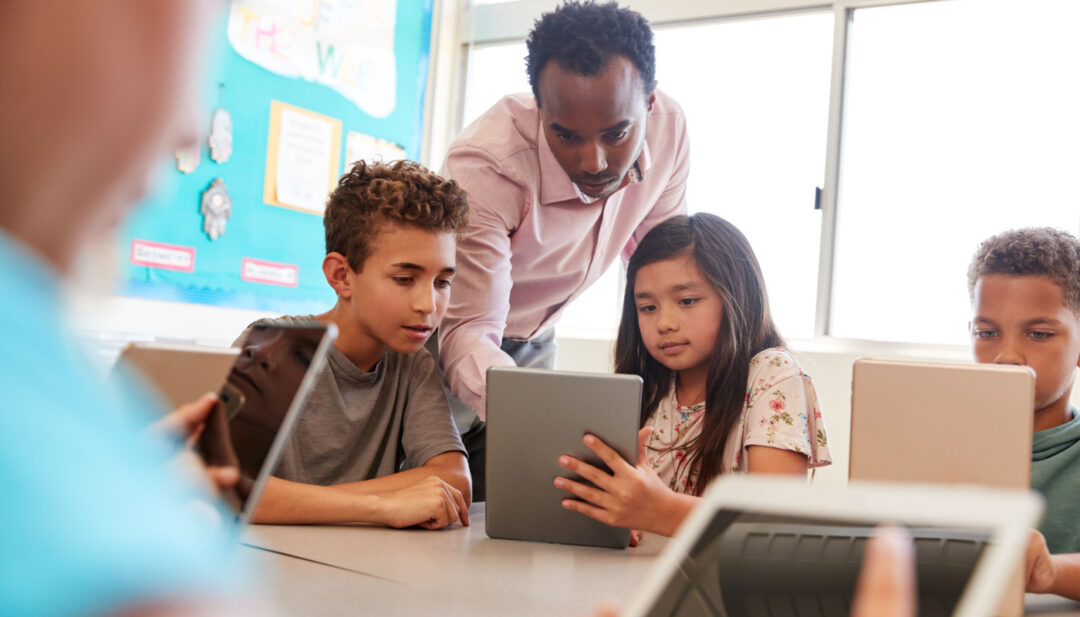 Teacher with school kids using computers in class; AI lesson plans concept