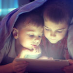 Two kids using tablet under a blanket at night; internet privacy lessons concept