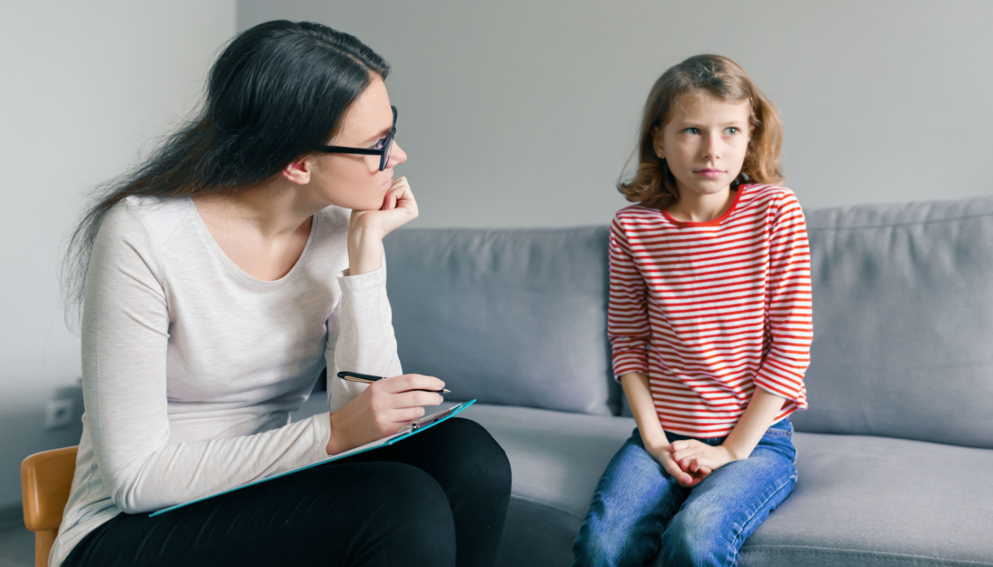 Anxious looking child next to adult seat in child-size chair, ready to take notes; school psychologists concept