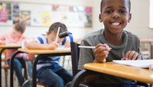 Pupil in wheelchair smiling at camera in classroom at the elementary school; special education directors concept
