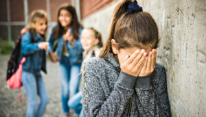 Crying girl being bullied at school; anti-cyberbullying concept